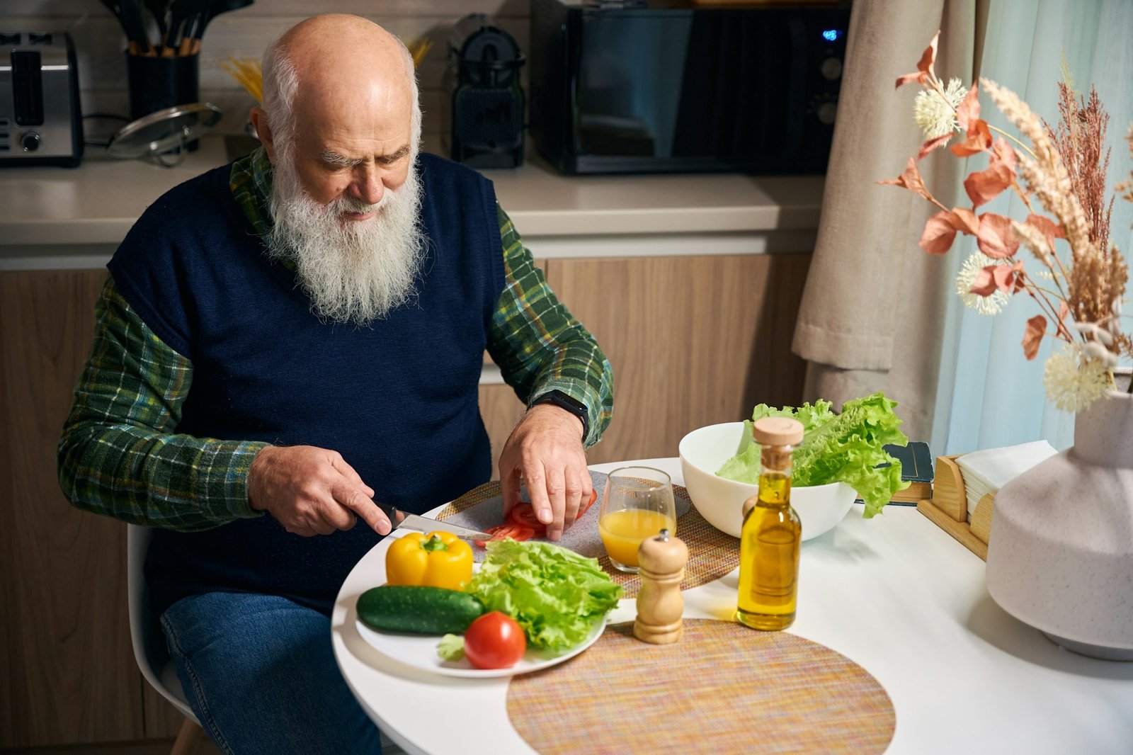 Old man at the kitchen table cuts vegetables for salad